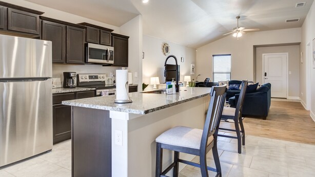 A modern kitchen with dark cabinets, stainless steel appliances, and a central island with bar stools. - Milano Guesthouse (Lubbock)