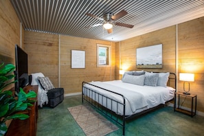 Quarto com cama, ventilador de teto, janela, ar condicionado fixado na parede e mesa de cabeceira com abajur.