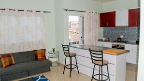 A modern kitchen with a central island, red cabinets, and a grey sofa with patterned cushions.