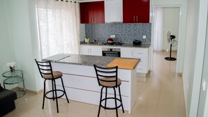 A kitchen with a central island, two bar stools, a small table, and a fan in the background.