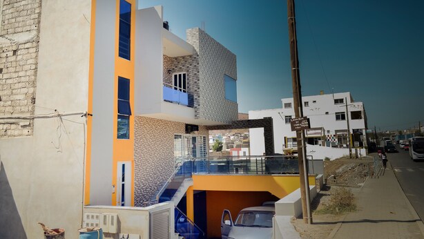A modern multi-story building with a mix of brick and smooth surfaces, a prominent yellow and blue facade, and a visible staircase leading to an upper level.