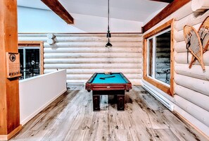 Enjoy a game of pool in this cabin-style room with a large window offering a view of the outdoors.