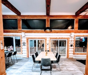 Cozy dining area with a long table and comfortable seating, surrounded by natural light and rustic charm.