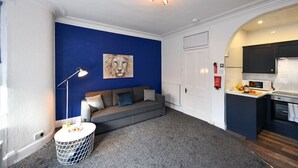 Un salon moderne avec un mur d’accent bleu, un canapé gris, une petite table ronde et un luminaire suspendu au plafond.