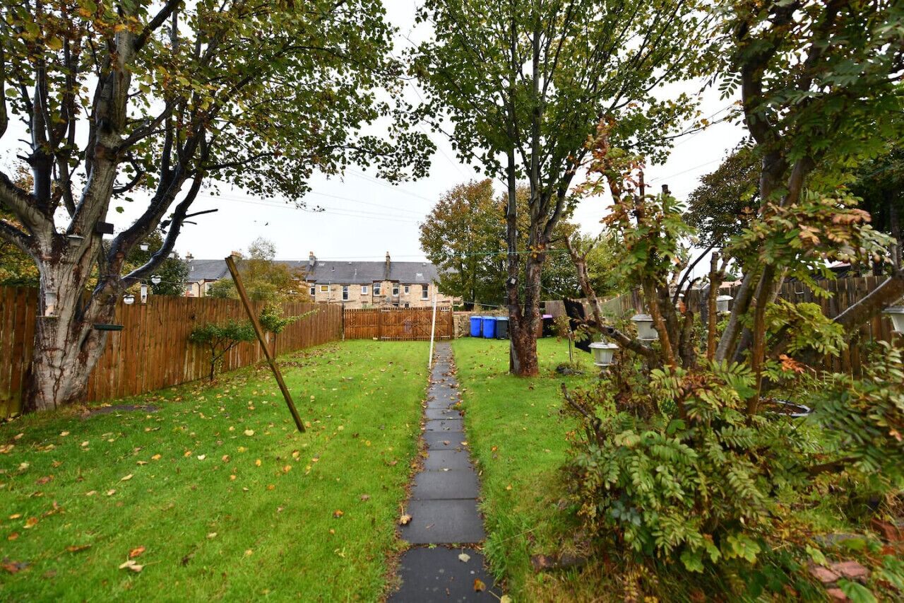 Un jardin à l’arrière de la maison, avec un chemin dallé menant à l’entrée.