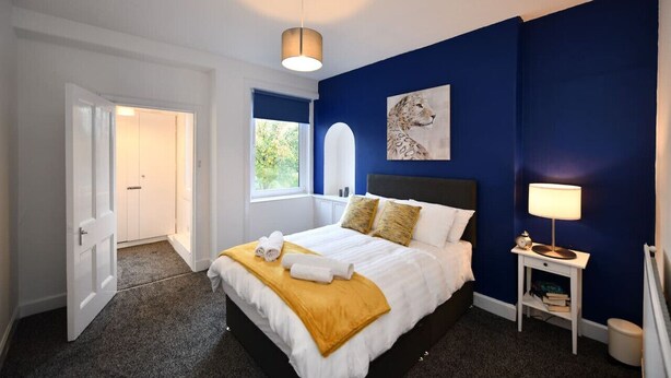 Une chambre à coucher avec un lit, une table de chevet, une lampe, un tableau et une fenêtre.
