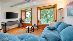 A modern living room with a sofa, a flat-screen TV, and a window seat with a view of trees. - Stunning Villa with infinity pool, Croatia (Donja Poljana)