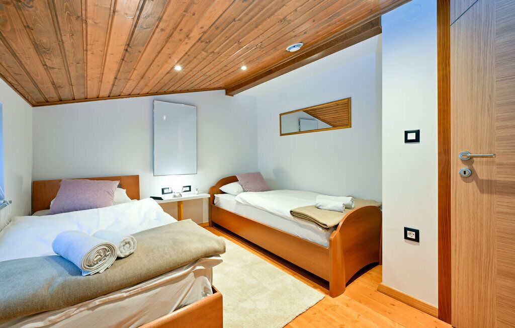 Een slaapkamer met een houten plafond, een groot bed, een kleiner bed, een nachtkastje, een spiegel en een kledingkast.