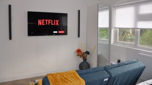 A modern living room with a large flat-screen TV mounted on the wall displaying 'NETFLIX'. - Beautiful and modern Studio flat in Milton Keynes (Milton Keynes)
