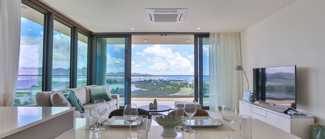 A modern dining area with a table set for two, large windows with a view of the landscape, and a television on the right.