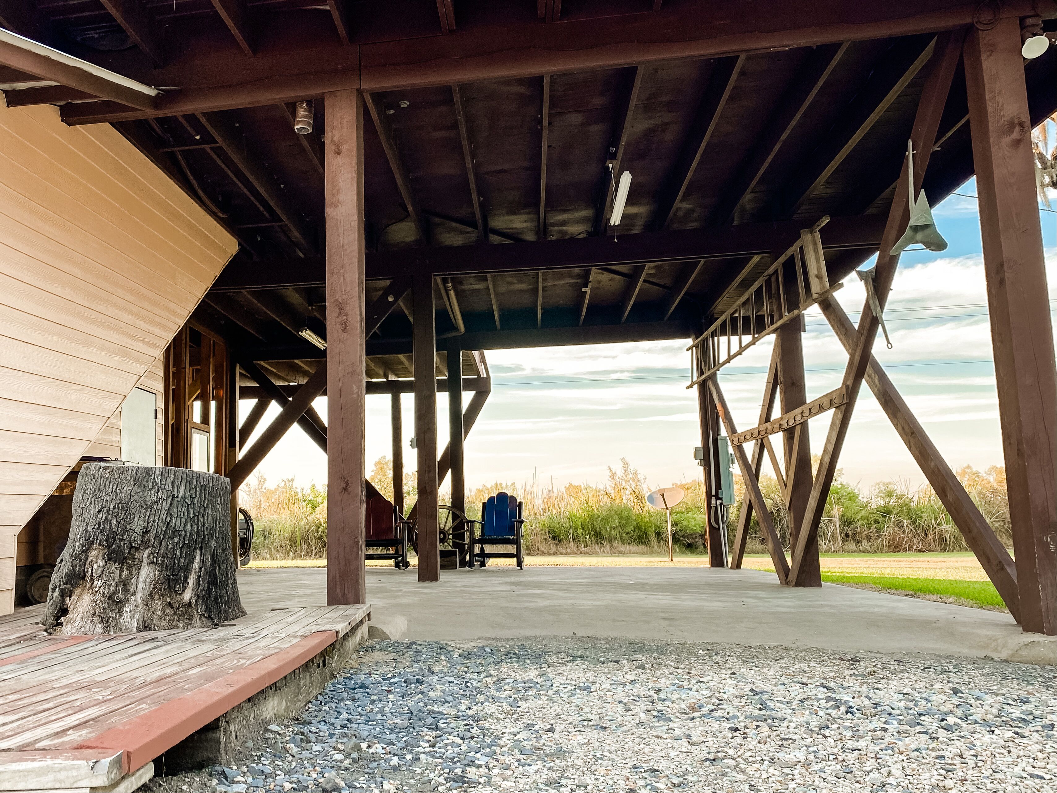 A covered outdoor area with a wooden deck, a large tree stump, and a view of the landscape.