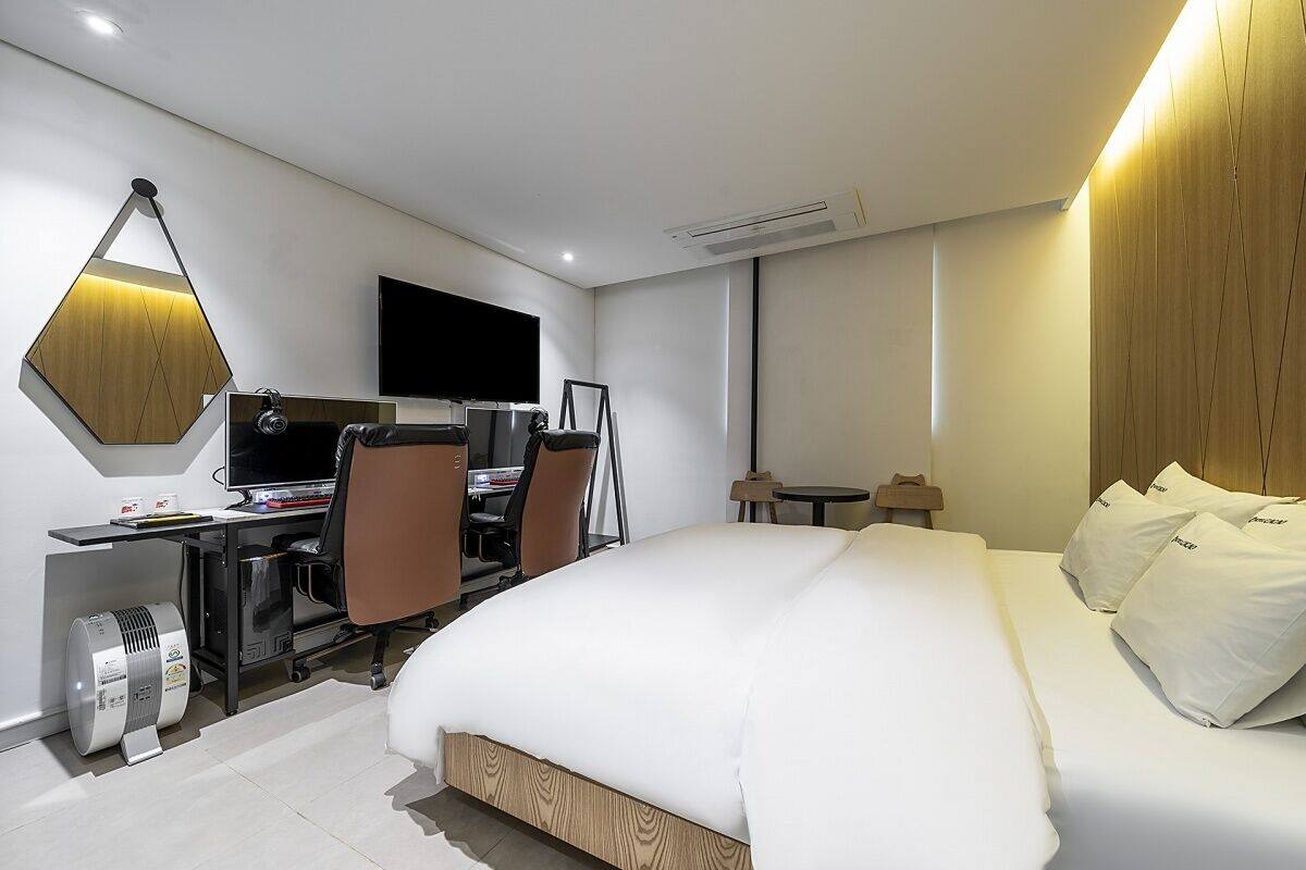 Moderni hotellihuone, jossa on suuri sänky, työpöytä tietokoneella, tuoli, televisio ja ainutlaatuinen kuusikulmainen valaisin.