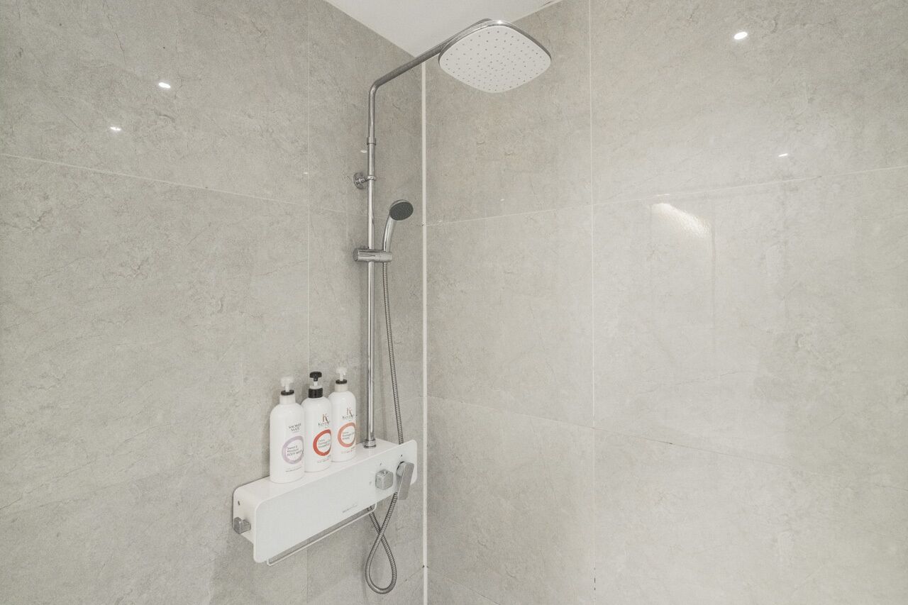 A modern bathroom with a shower, a control panel, and two bottles of shampoo.