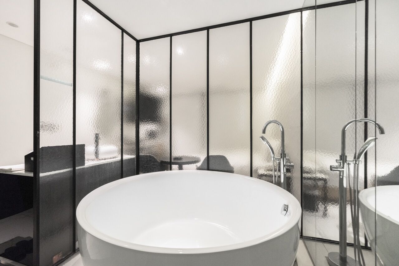 Un baño moderno con una bañera independiente grande, un lavamanos separado y un separador de vidrio.