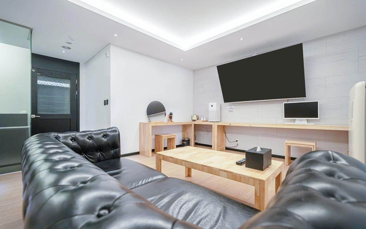 Una sala de estar moderna con un sofá de cuero negro, una mesa de centro de madera y un televisor de pantalla plana montado en la pared.