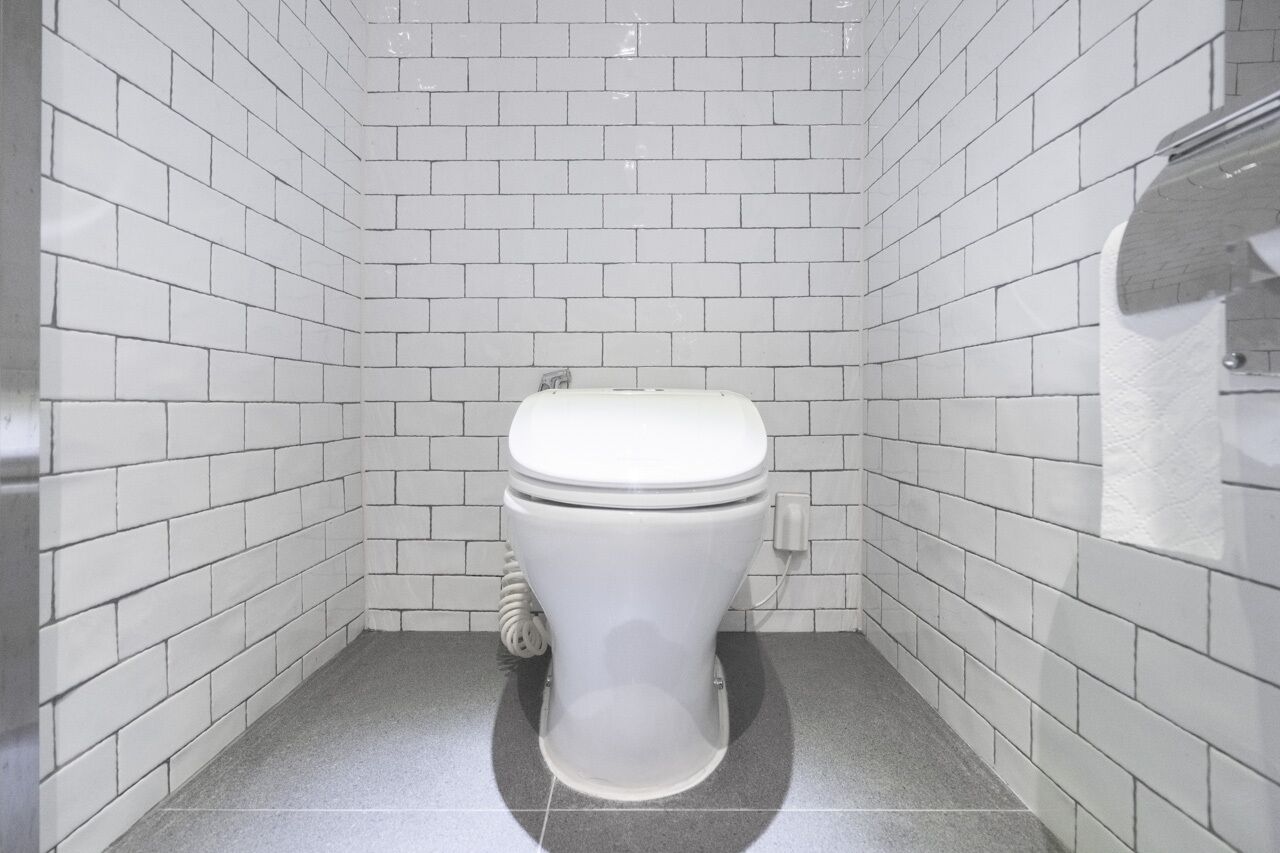 A small, white-tiled bathroom with a white toilet and a visible pipe.