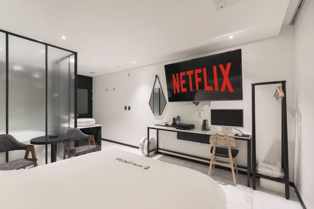 Moderni hotellihuone, jossa on suuri sänky, työpöytä tietokoneella, seinälle asennettu televisio ja oleskelualue tuoleineen.