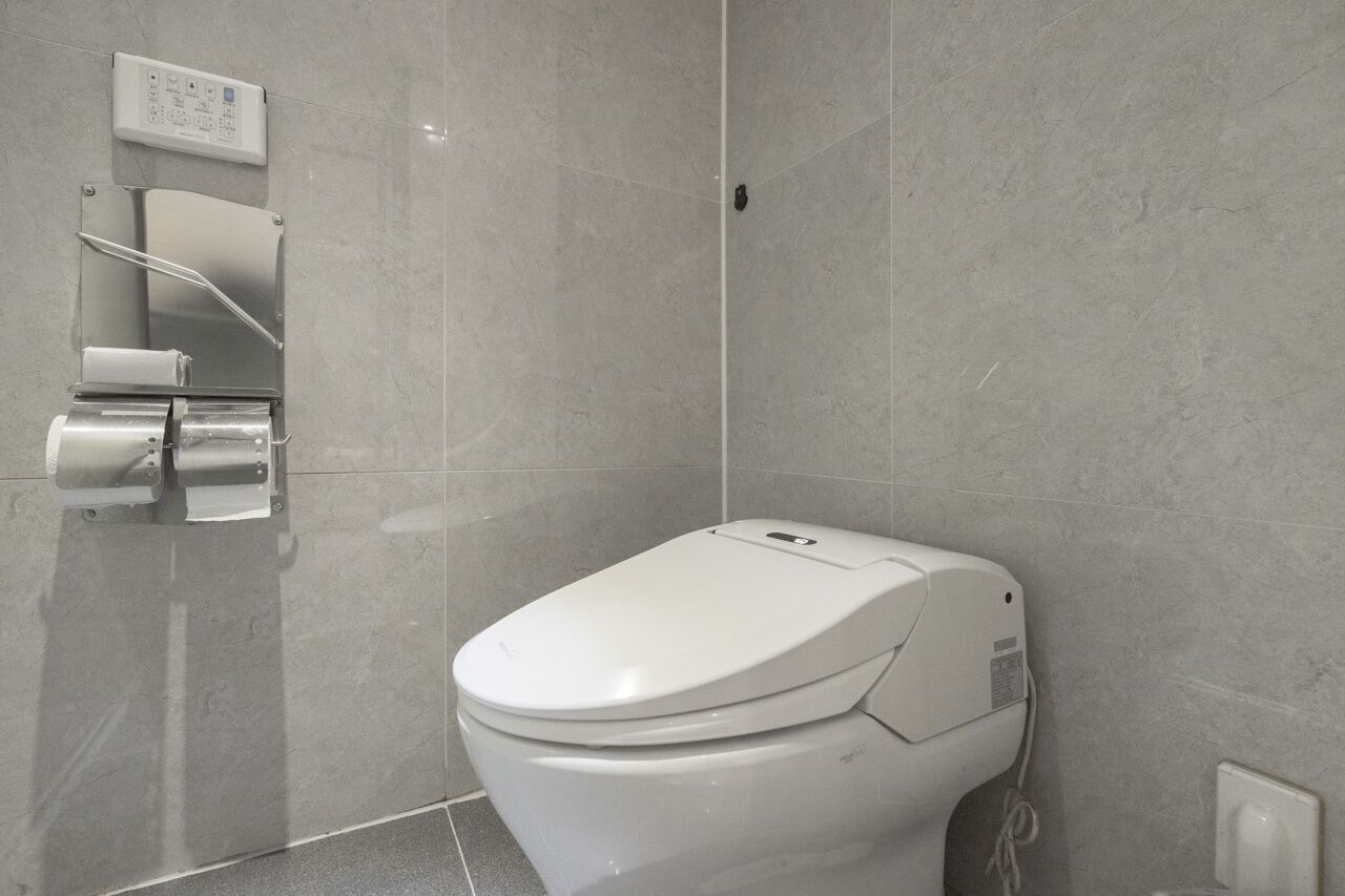 A modern bathroom with a white toilet, a wall-mounted bidet, and a control panel.