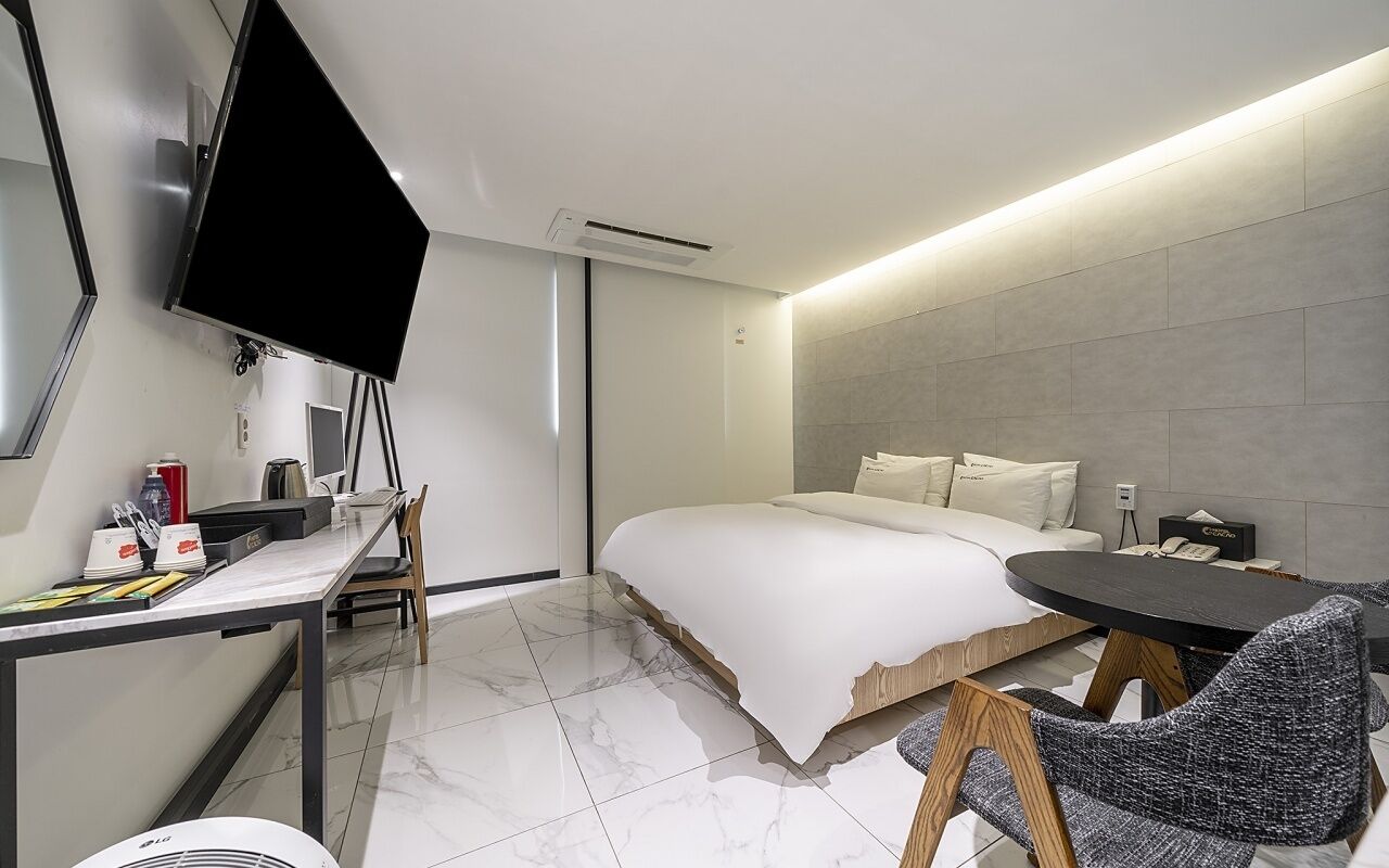 Una habitación de hotel moderna con una cama, un escritorio con televisor de pantalla plana, una silla y una mesita.