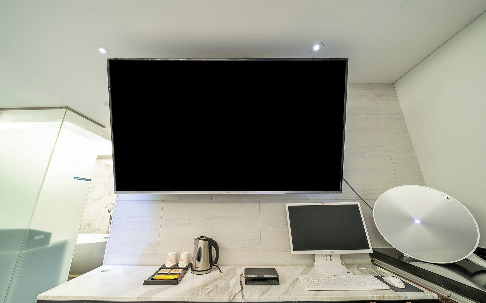 Habitación de hotel moderna con un televisor de pantalla plana grande, un monitor más pequeño, un escritorio con teclado, ratón y una cafetera.