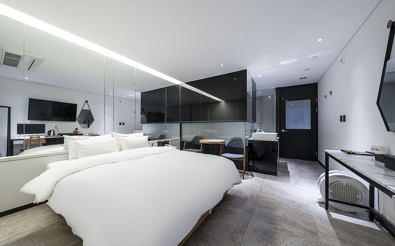 Una habitación de hotel moderna con una cama grande, un escritorio, una silla, un televisor y un espejo amplio.