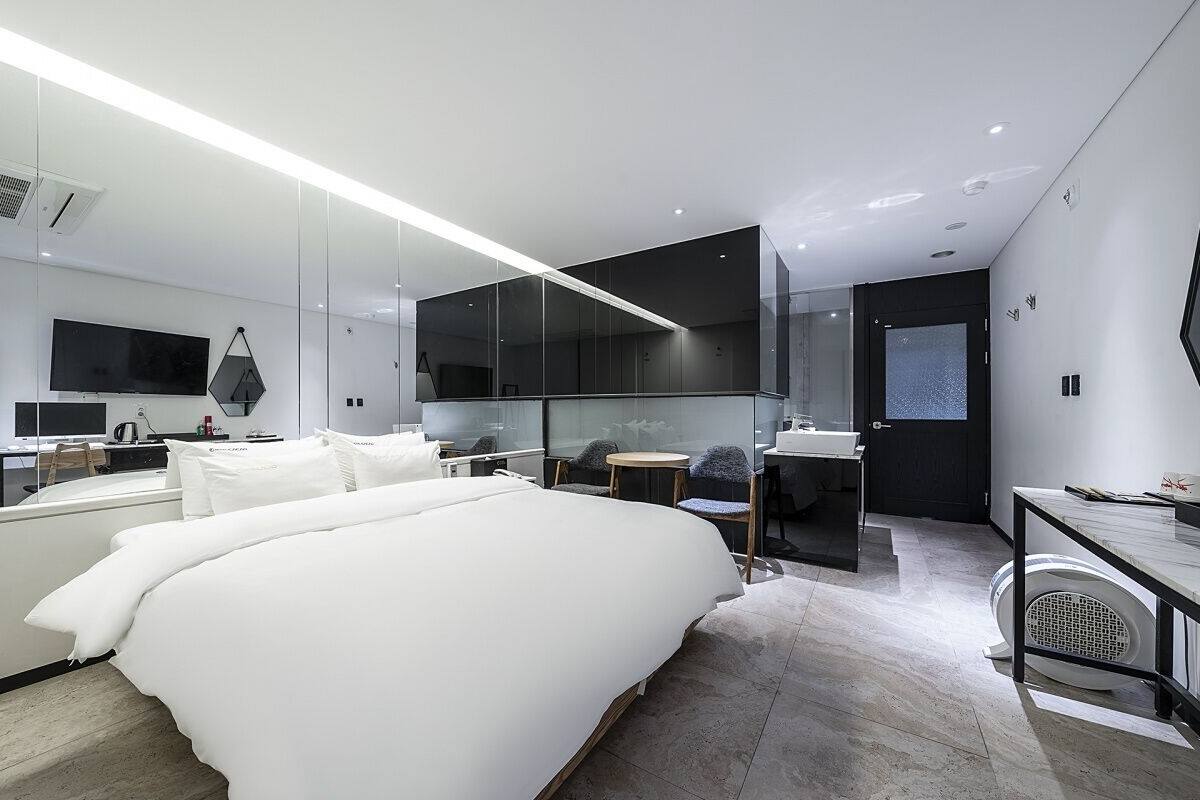 Moderni hotellihuone, jossa on suuri sänky, työpöytä, tuoli, televisio ja suuri peili.