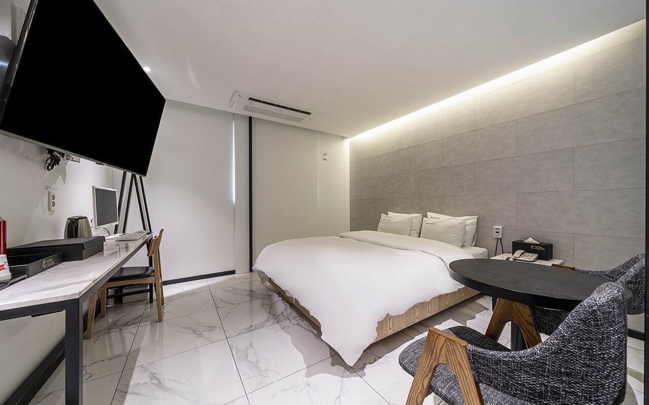 Una habitación de hotel moderna con una cama, un escritorio con una computadora, una silla y una mesita.