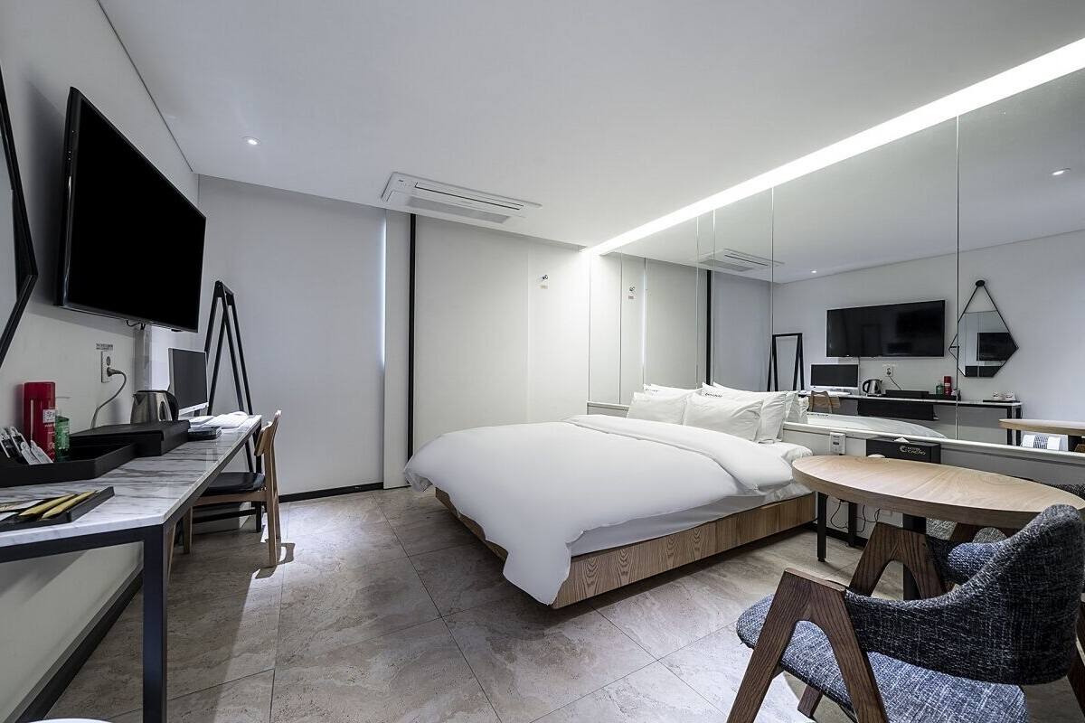 Moderni hotellihuone, jossa on sänky, työpöytä, tuoli, televisio ja suuri peili.
