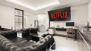 Een moderne woonkamer met een zwarte leren bank, een flatscreen televisie en een keukenhoek met een koffieapparaat.