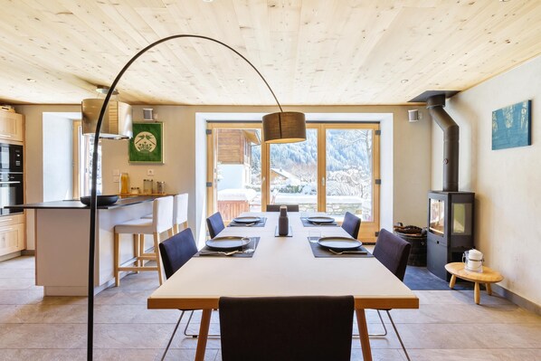 A modern kitchen with a dining area, wooden ceiling, and large windows.