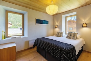 Une chambre à coucher avec un lit, deux fenêtres, un plafond en bois, un tableau accroché au mur et une lampe de chevet.
