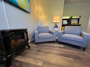 Una sala de estar con chimenea, dos sillones, una lámpara y una consola de videojuegos.