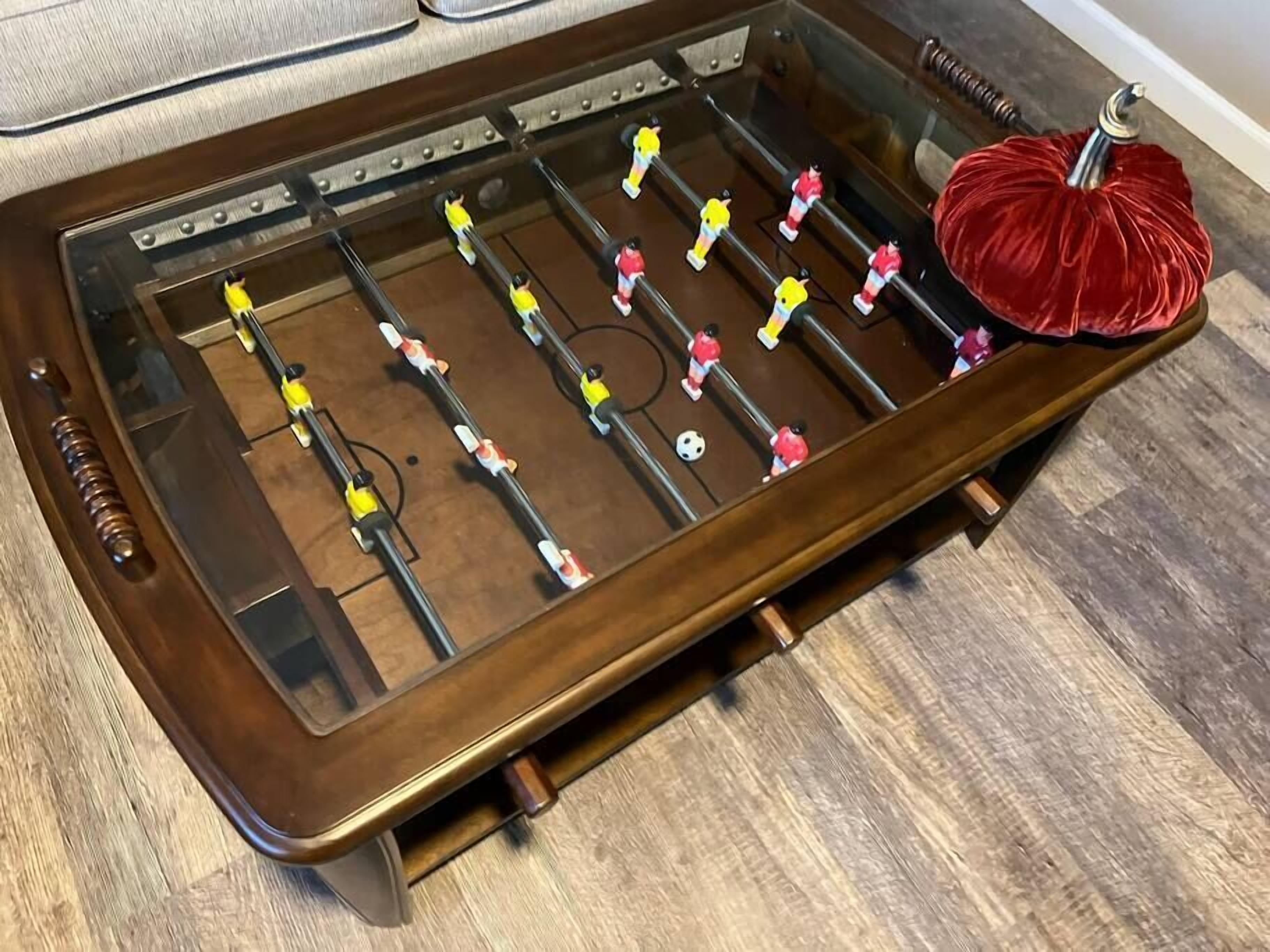 A wooden foosball table with a red pom-pom on one end.