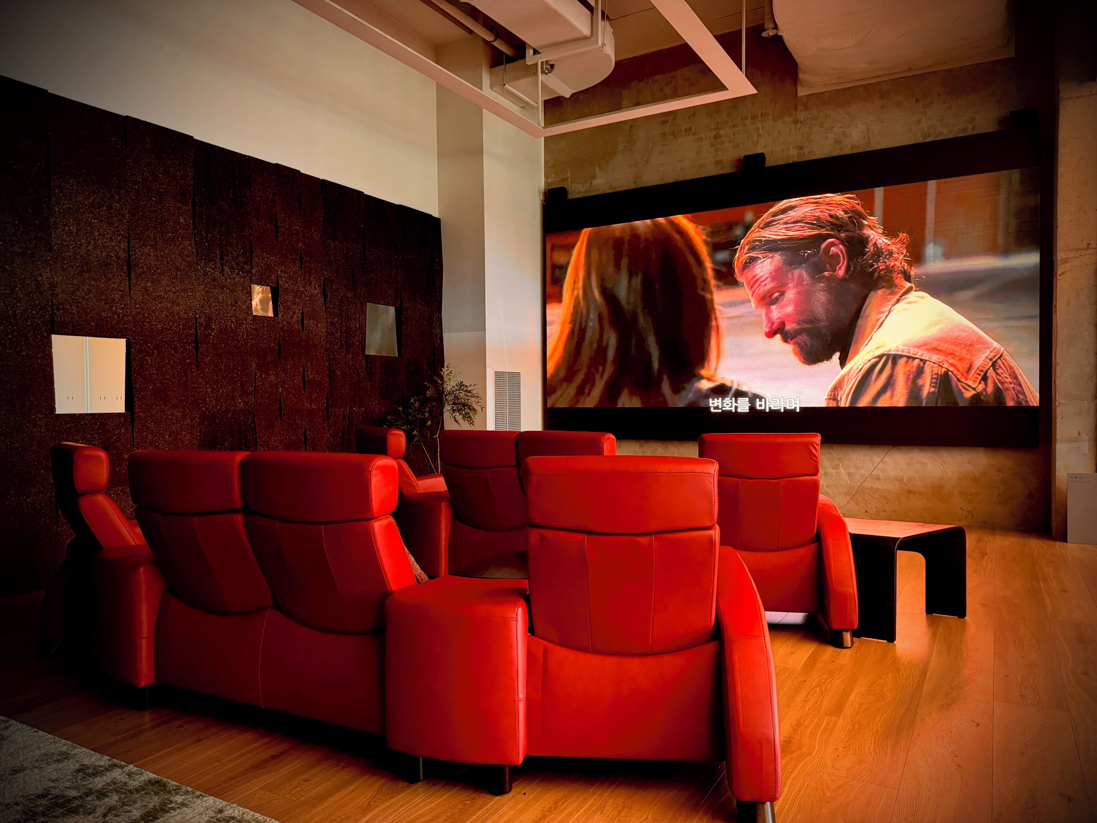 Una sala de cine con asientos reclinables rojos, una pantalla grande y una pared de ladrillo.