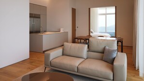 A modern living room with a sofa, a dining area with a table and chairs, a kitchen area, and a large window offering a view. - The Heaven Resort (Ansan)