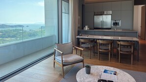 A modern kitchen with a large island, a dining area with chairs, and a view of a landscape through large windows. - The Heaven Resort (Ansan)