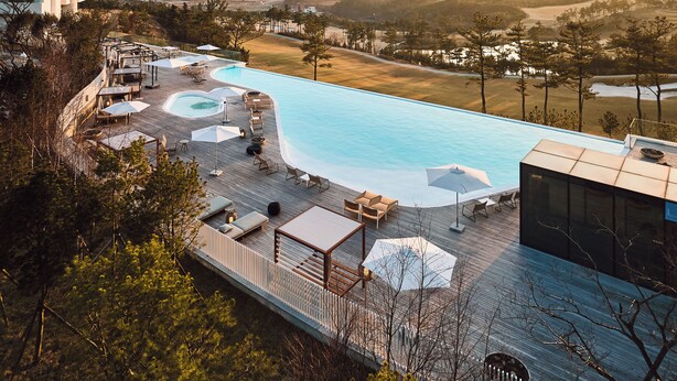 A rooftop pool area with multiple seating arrangements, including lounge chairs and umbrellas, surrounded by a wooden deck and overlooking a scenic landscape. - The Heaven Resort (Ansan)