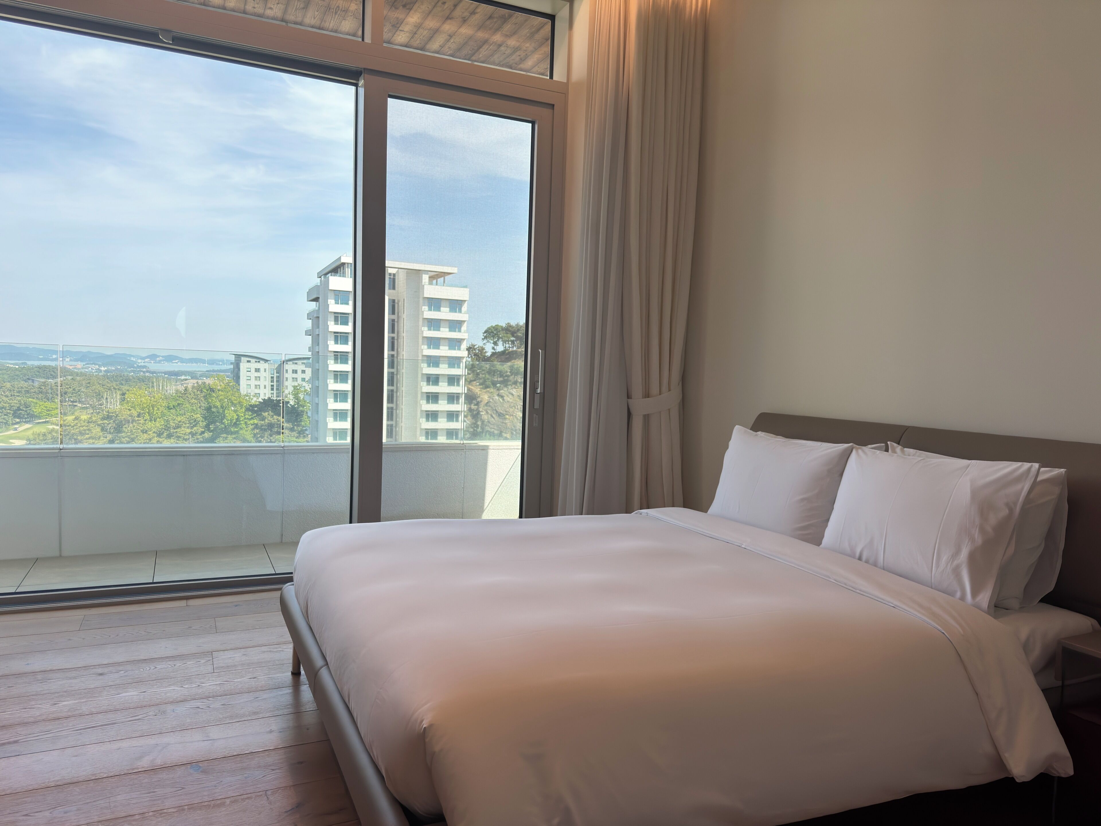 A hotel room with a large bed, a view of buildings, and a balcony.