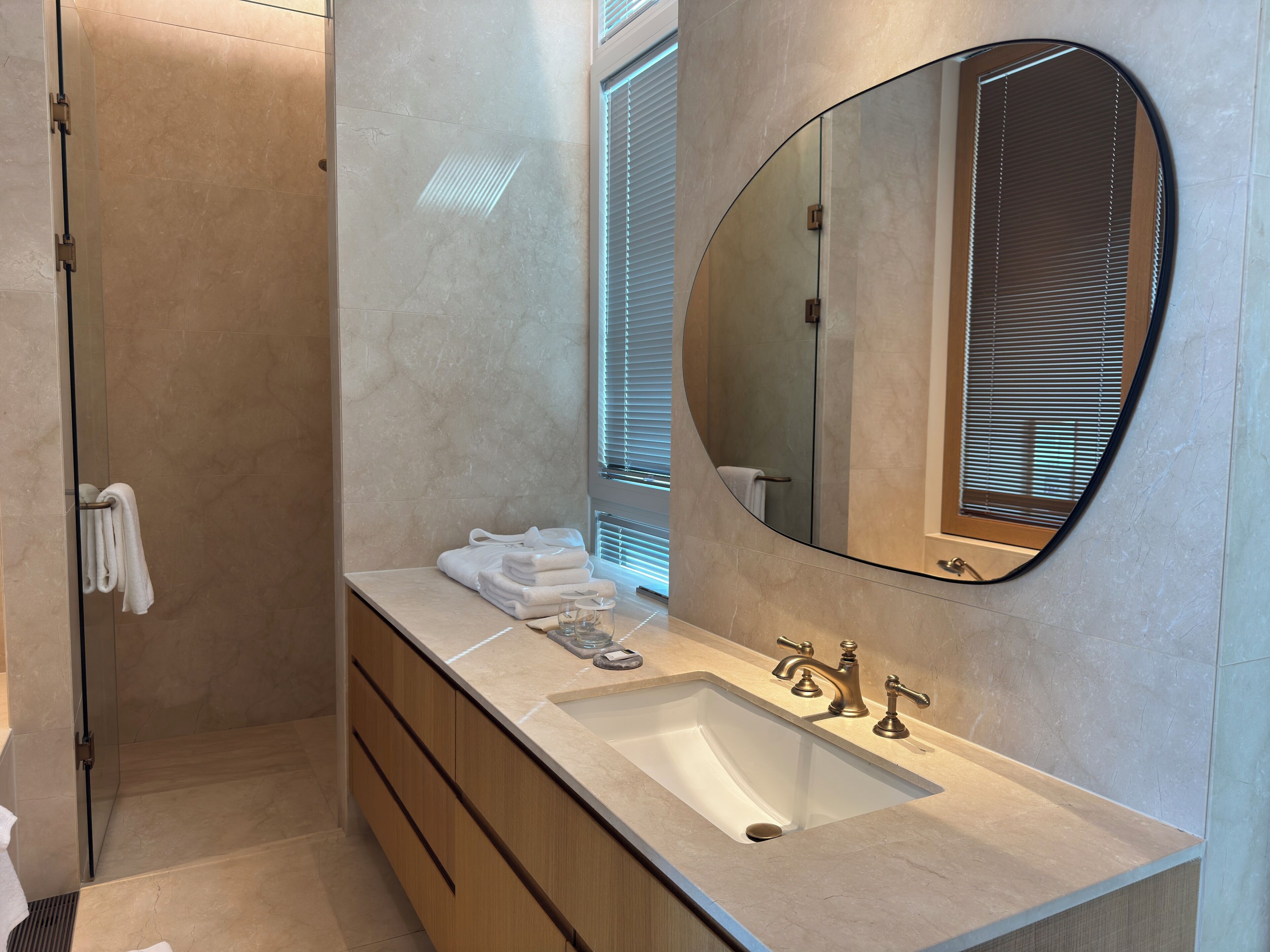 Un baño moderno con un espejo ovalado grande, un lavamanos con dos grifos y un perchero con toallas dobladas.