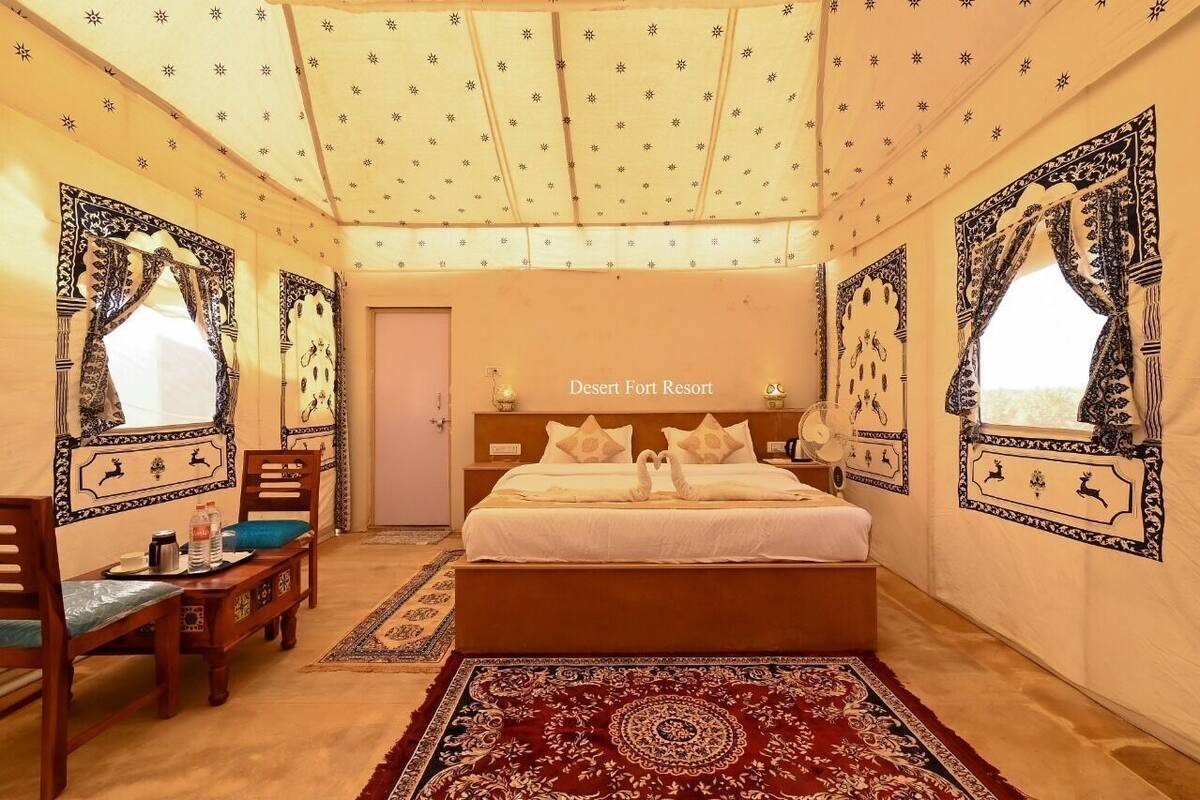 Un dormitorio con una cama, una mesita de noche, una mesa con sillas y una alfombra estampada.