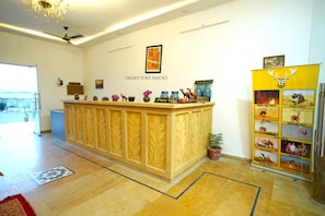 A reception desk with a sign reading 'Desert Fort Resort,' a chandelier, and a bulletin board with safari images. - Desert Fort Resort (Jaisalmer)