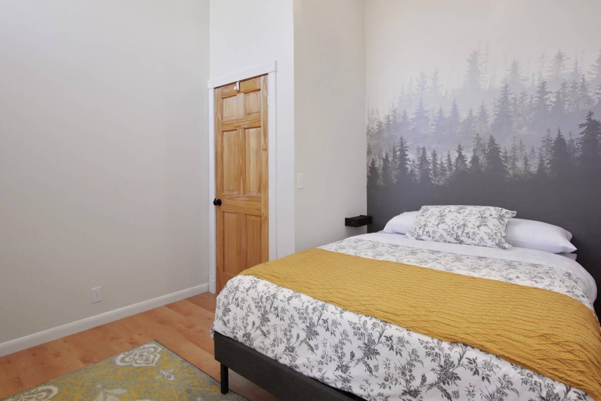 Un dormitorio con una cama, una puerta de madera y un mural de un bosque en la pared.