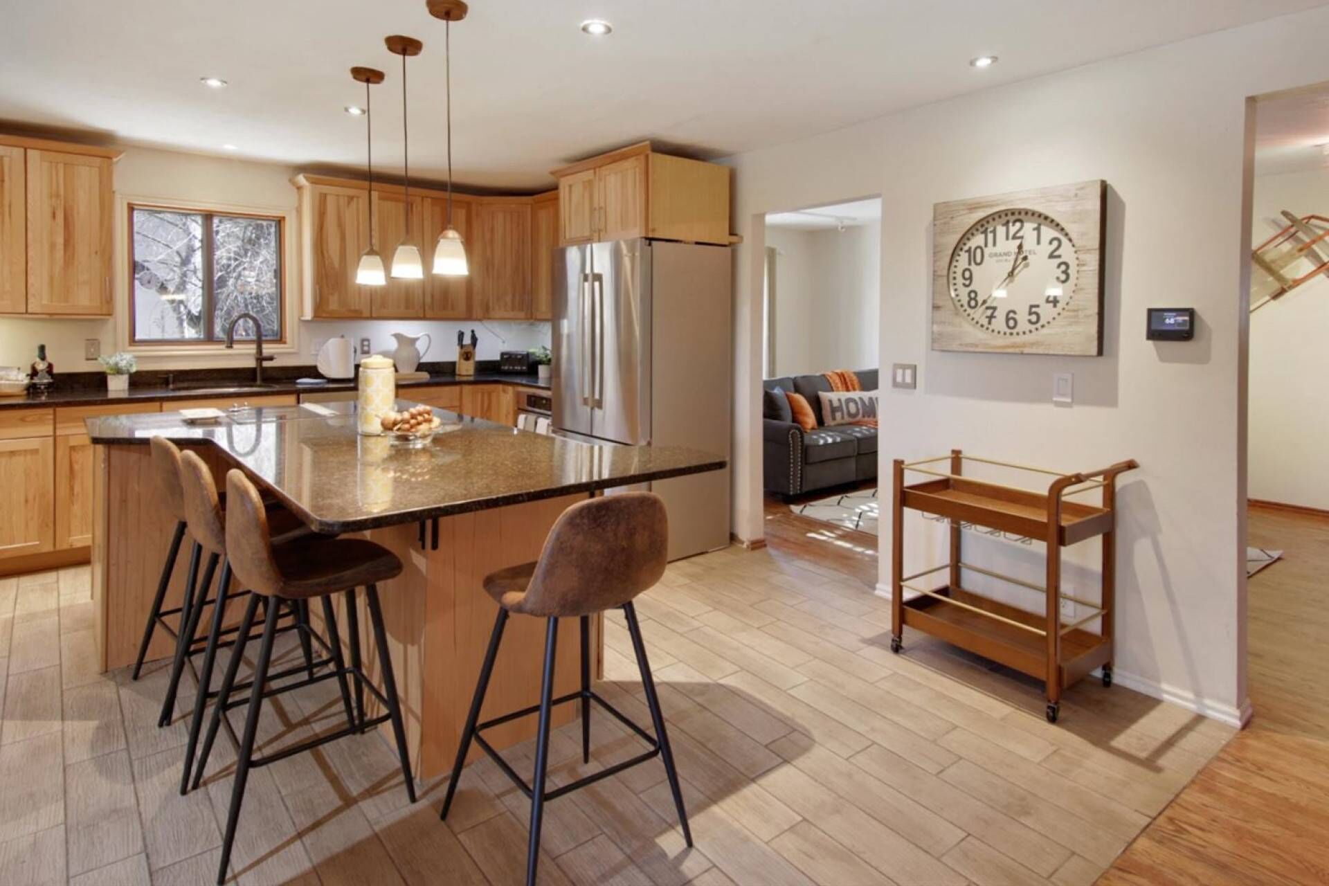 A modern kitchen with wooden cabinets, a large island with bar stools, stainless steel appliances, and pendant lighting.