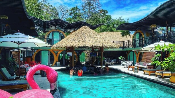 A pool area with lounge chairs, a thatched-roof structure, and flamingos. - Saranda Boutique Hotel (Cahuita)