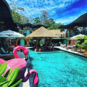 A pool area with lounge chairs, a thatched-roof structure, and flamingos. - Saranda Boutique Hotel (Cahuita)