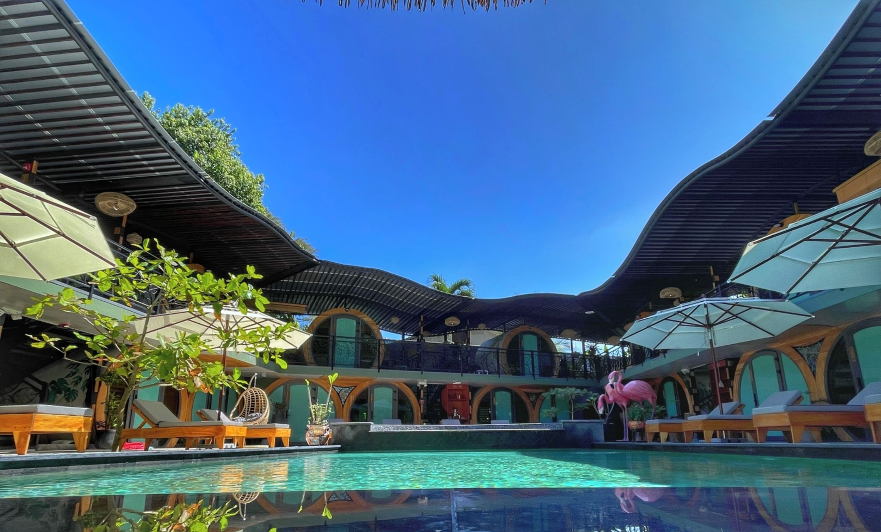 A pool area with lounge chairs and umbrellas, surrounded by a covered walkway with a curved roof.