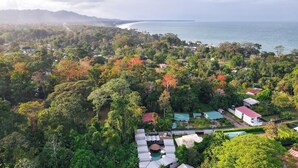 An aerial view of a resort with multiple buildings surrounded by dense forest, a swimming pool, and a view of the ocean. - Saranda Boutique Hotel (Cahuita)