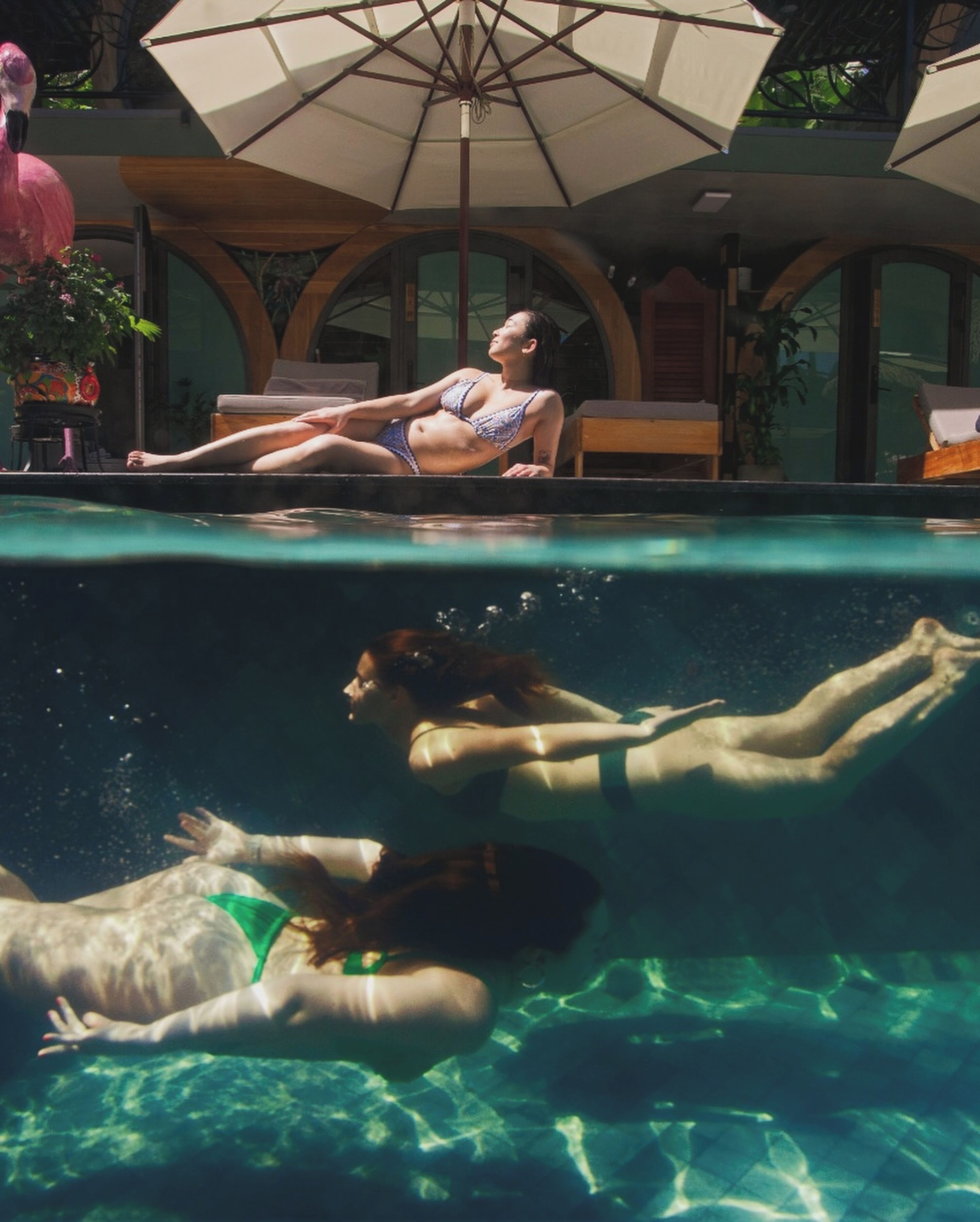 A swimming pool with a person lying on the edge and another person swimming underwater.