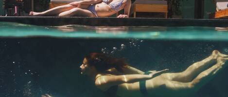 A swimming pool with a person lying on the edge and another person swimming underwater.