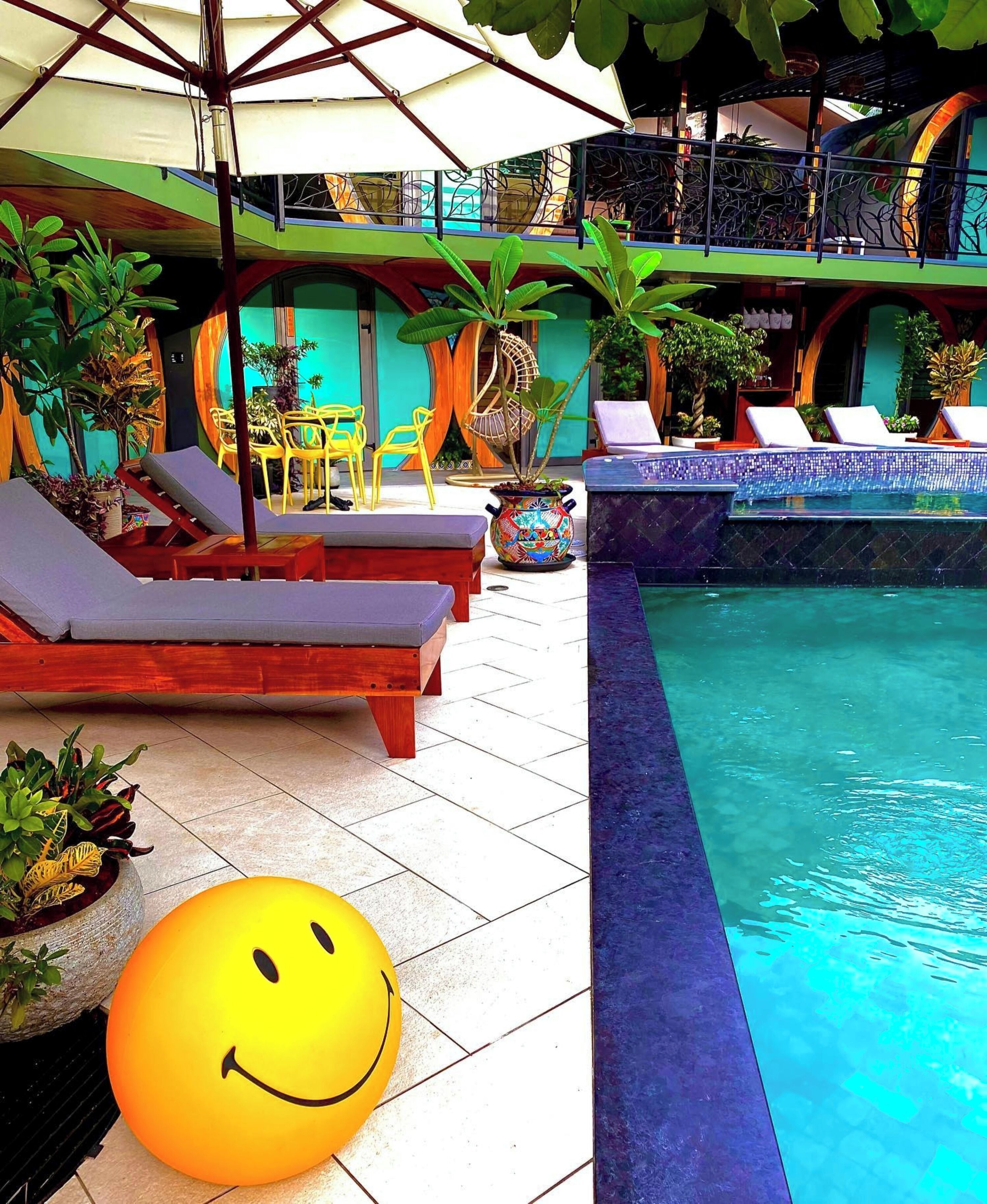 A pool area with lounge chairs, a large smiley face decoration, and potted plants.